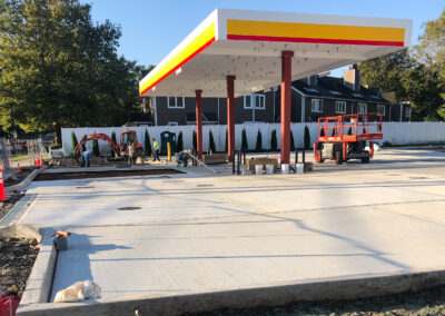 Commercial masonry construction site of a gas station drive-through lane, concrete paving and concrete curb around the perimeter, extensive drainage, orange excavator sitting on site.