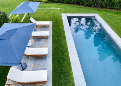 Contemporary, minimalist residential pool renovation with stone coping surrounded by grass alongside small stone pool patio.