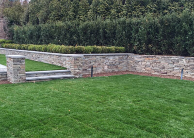 Modern residential patio and surround renovation features stacked stone retaining wall and steps with stone coping.