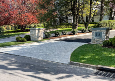 Asphalt paving driveway with mounted stone columns, block border, decorative entrance pattern and band detail, and drains.