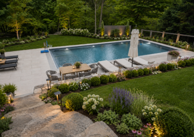 Luxury estate backyard showcasing custom stone steps, a structural stone retaining wall, and a large paver pool patio surrounded by lush, manicured landscaping.