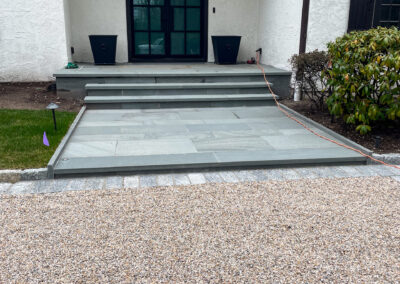Modern residential front entrance renovation with polished stone walkway and steps to front door, gravel paved driveway.