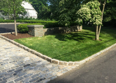 Contemporary block paving entrance and asphalt paving driveway renovation with block border, stacked stone retaining wall.