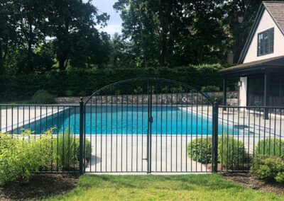Modern residential pool renovation, polished stone pool patio with decorative band detail and sleek black entrance gate.
