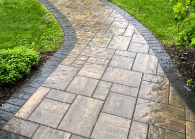 Modern stone walkway in random pattern with polished decorative band detail leading to driveway.
