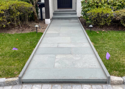 Modern residential front entrance renovation with polished stone walkway and steps to front door, gravel paved driveway.