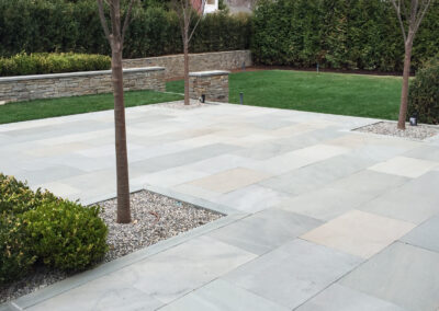 Modern minimalist residential patio and surround renovation features stone patio and tree plantings with stone border.
