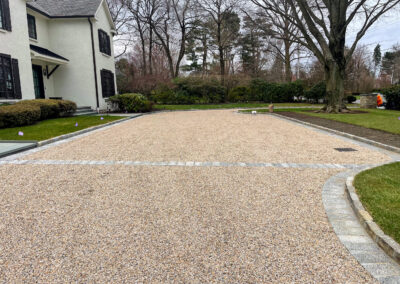 Contemporary, minimalist residential gravel driveway renovation with block border, decorative band details, and drains.
